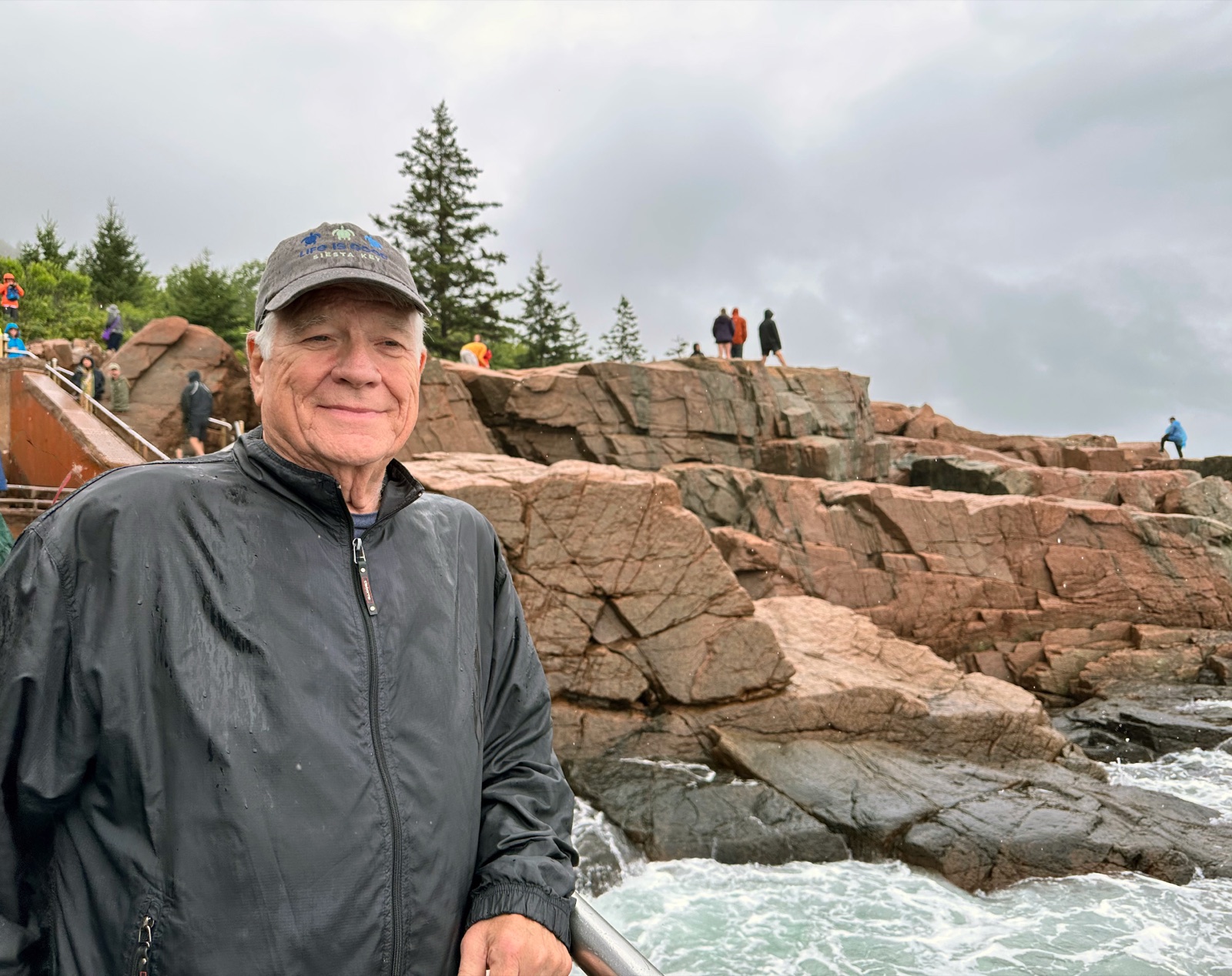 Paul Eric Anderson in a rain jacket, smiling on a rocky stretch of coastline